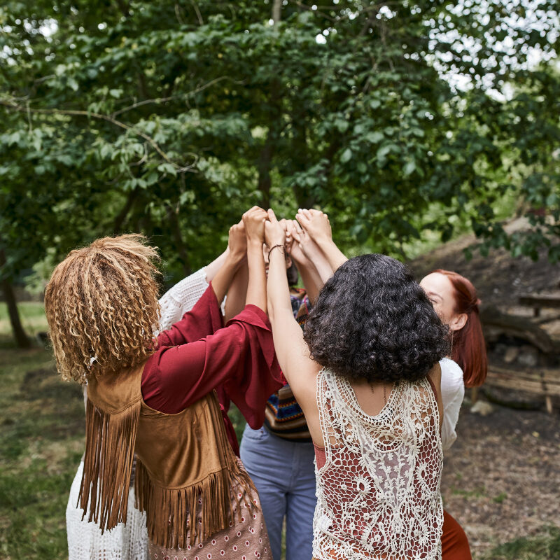AVMH-MentalHealthtreatments trendy multiethnic girlfriends in boho clothes holding hands outdoors in retreat center