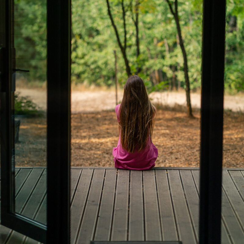 AspenView-Anxiety a young smiling woman sits sideways on a terrace overlooking the forest and enjoys the silence