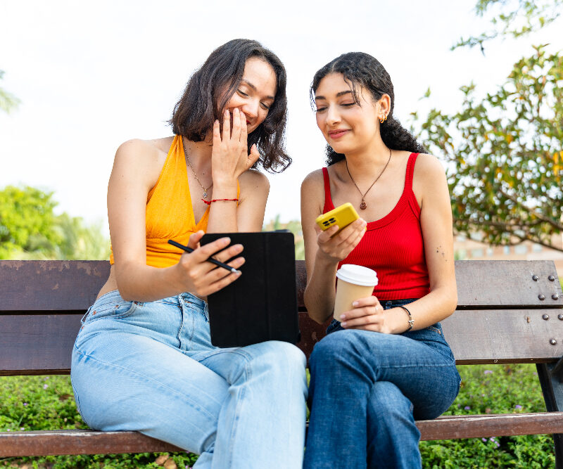 Two interracial friends use a tablet to draw in the park two friends talking about ADHD treatment from Aspen View Mental Health in Greeley, Colorado.