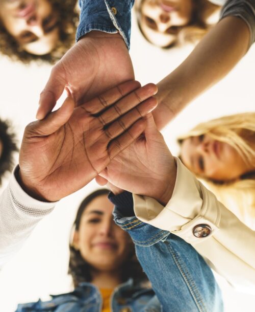 From below of group of content multiracial friends joining hands together and standing in circle